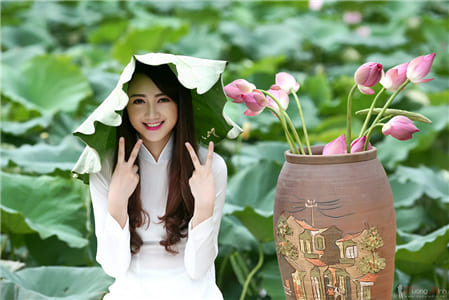 Hình ảnh cô gái xinh đẹp với tà áo dài trắng bên cạnh những bông hoa sen và đội lên đầu chiếc lá sen